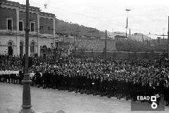 Persone ragazze e dirigenti di colonia nel piazzale davanti ad un edificio.
[Foto scattata in Piazza Vittorio Veneto, sulla sinistra l'edificio  la stazione ferroviaria di Salerno. Nota a cura di Anna De Falco]