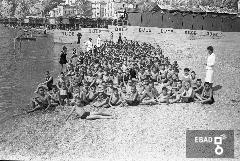 Bambini ed educatrici al mare e sullo sfondo vista degli stabilimenti balneari ed abitazioni circostanti.
La foto  stata scattata a Salerno nel 1937-1943 da una barca antistante lo stabilimento balneare Mussolini della colonia marina Mussolini. Stabilimento situato immediatamente ad ovest del molo 3 gennaio che si trovava alle spalle del fotografo. Oggi il luogo risulta profondamente cambiato e l'asfalto ha sostituito la spiaggia. Nota a cura di Massimo La Rocca]